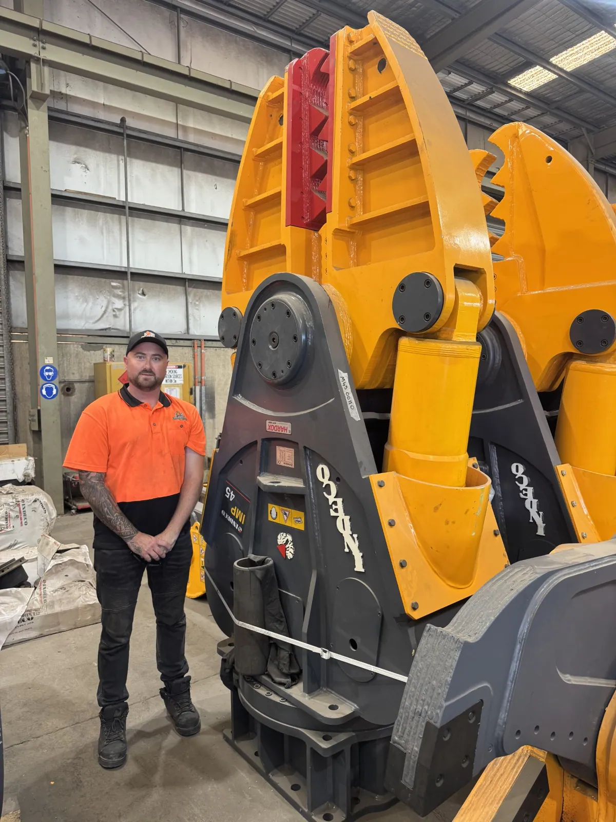 JW Hydraulics & Mechanical staff member in branded hi-vis beside a large Indeco IMP 45 hydraulic pulveriser in the Queanbeyan workshop