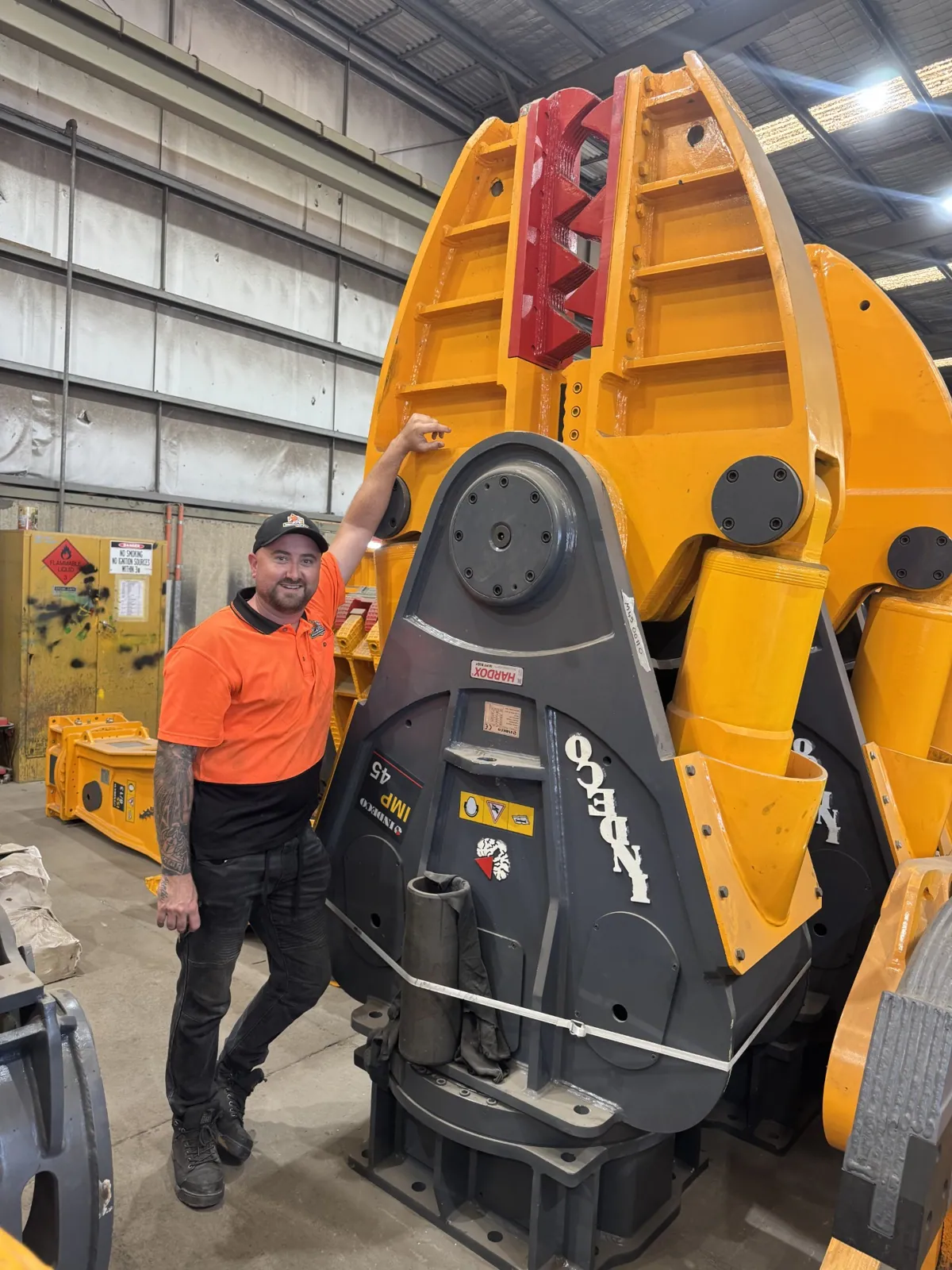 JW Hydraulics & Mechanical staff member beside a large Indeco hydraulic breaker attachment in the workshop